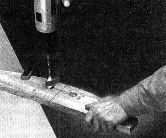 Изготовление ручки для переноски кресла в обрамлении спинки: сверлим два отверстия диаметром 25 мм и вырезаем лобзиком лишнее